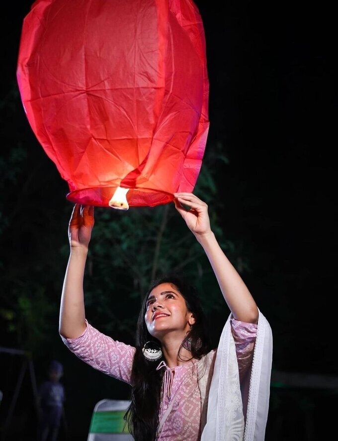 Photo of Releasing paper lanterns into night sky whhile the couple sits on  the feras